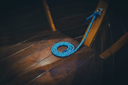 closeup of blue rope arranged in a spiral shape on the wooden brown deck of a sailing yacht