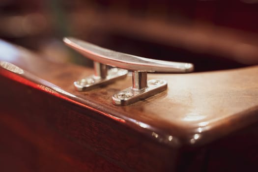 closeup with selective focus on piece of marine cleat equipment on brown wooden boat yacht