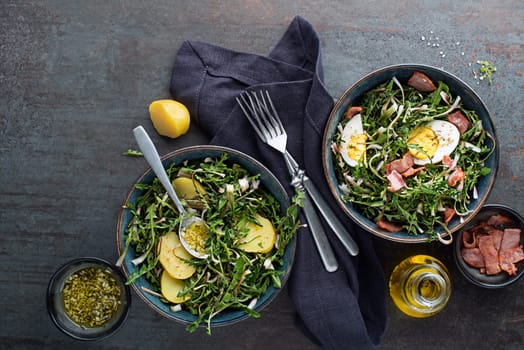 Dandelion salad with potato eggs and bacon on grey background.