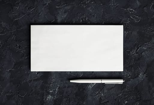 Photo of blank paper envelope and pen on black plaster background. Blank stationery template. Top view.