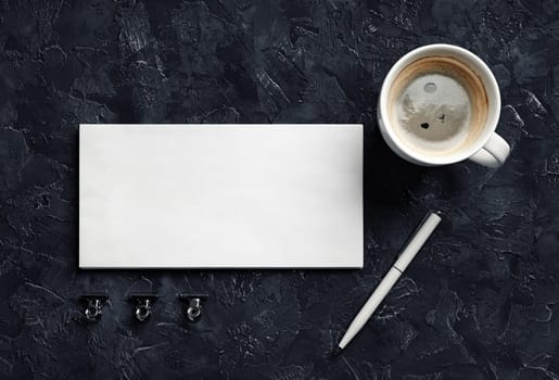 Blank envelope, coffee cup, pen and metal clips on black plaster background. Branding mock up. Top view.