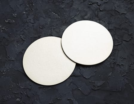 Blank white beer coasters on black plaster background.