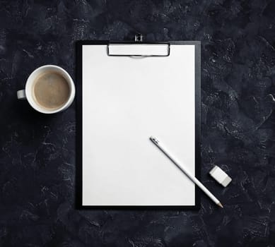 Clipboard with blank letterhead, coffee cup, pencil and eraser on black plaster background. Top view.