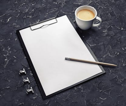Clipboard with blank letterhead, pencil, coffee cup and metal clips on black plaster background. Responsive design template.