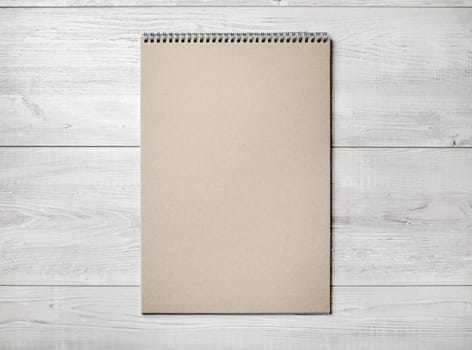 Photo of blank kraft sketchbook on light wooden background. Flat lay.