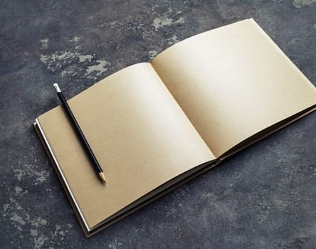 Open blank craft paper brochure and pencil on concrete background. Branding mock up.
