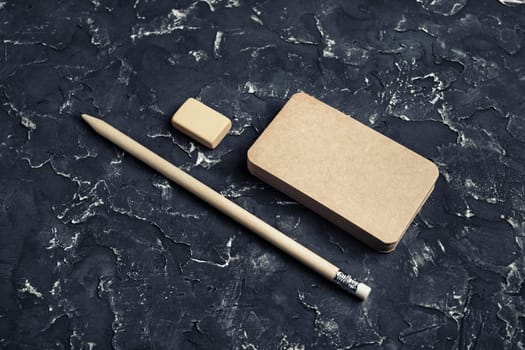 Photo of blank kraft business card, pencil and eraser on black plaster background.