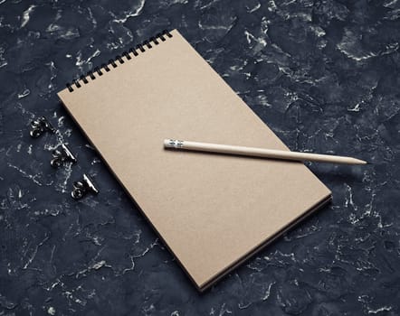 Blank kraft note pad and pencil on black plaster background. Responsive design mockup.