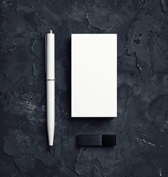 Blank business cards, pen and usb flash drive on black plaster background. Responsive design template. Top view.