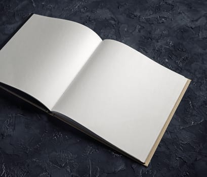 Photo of blank opened notebook on black plaster background. Template for graphic designers portfolios.