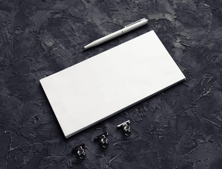 Blank envelope, pen and metal clips on black plaster background. Branding mock up.