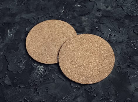 Photo of blank cork beer coasters on black plaster background.