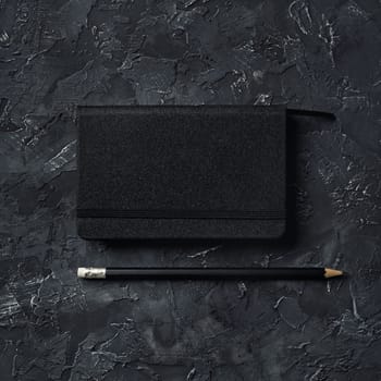 Blank black notebook and pencil on black plaster background. Responsive design mockup.