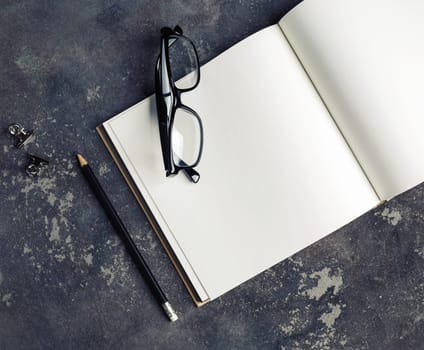 Photo of blank booklet, pencil and glasses on concrete background. Responsive design mockup. Stationery elements. Top view.
