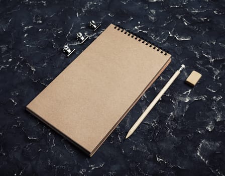 Photo of blank kraft notepad, pencil and eraser on black plaster background. Responsive design mockup. Template for placing your design.