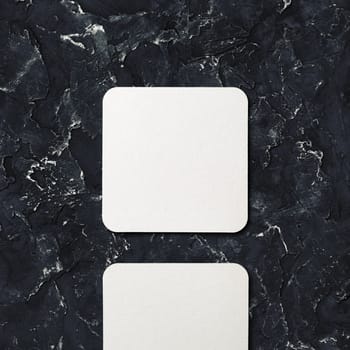 Photo of blank square beer coaster on black plaster background. Blank template for your design. Top view.