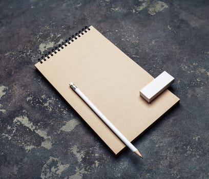 Photo of blank kraft notepad, pencil and eraser on concrete background. Template for placing your design.