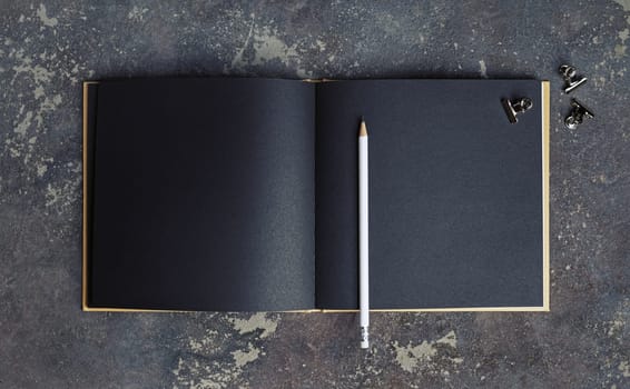 Blank black paper book, pencil and clips on concrete background. Responsive design template. Top view.