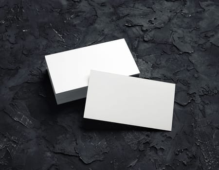 Photo of blank business cards on black plaster background. Mock-up for branding identity. Studio shot.