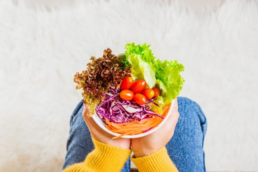Female hands holding bowl with green lettuce salad on legs, Above young woman eating fresh salad meal vegetarian spinach in a bowl, Clean detox healthy homemade food concept