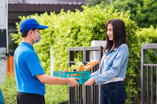 Asian young delivery man wear face mask making grocery fast service giving fresh food vegetable in plastic basket to woman customer receive at house door after pandemic coronavirus, Back to new normal