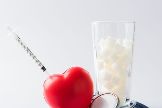 A glass full of white sugar cube sweet food ingredient and doctor stethoscope, studio shot isolated on white background, health high blood risk of diabetes and calorie intake concept and unhealthy drink