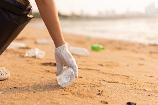 Volunteer woman picking plastic bottle into trash plastic bag black for cleaning the beach, female clean up garbage at sunset, Ecology concept and World Environment Day, Save earth concept