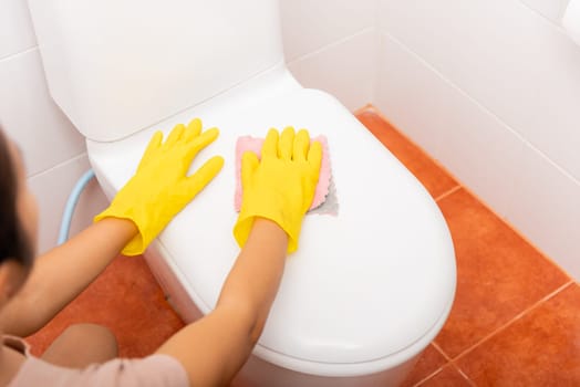 Hands of Asian woman cleaning toilet seat by pink cloth wipe restroom at house, female wearing yellow rubber gloves she sitting and cleanup or washing bathroom, Housekeeper healthcare concept
