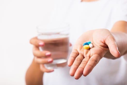 Closeup young Asian woman hold pill drugs in hand ready take medicines with a glass of water, studio shot isolated on white background, Healthcare and medical pharmacy concept