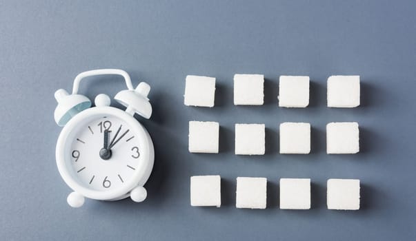 White sugar cube sweet food ingredient geometry pattern and alarm clock, studio shot isolated on a gray background, Minimal health high blood risk of diabetes and calorie intake concept