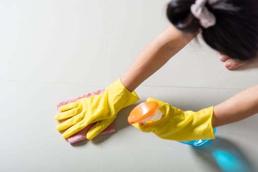 Asian woman wearing yellow rubber glover with cloth rag and detergent spray cleaning floor at home in living room, Female hands washing cleaner house worker, housework and housekeeping concept