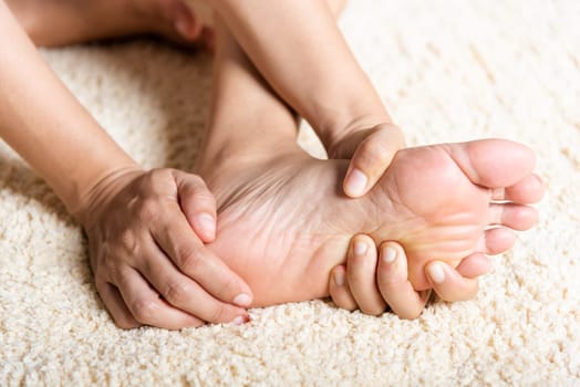 Foot pain, Asian woman feeling pain in her foot at home, female suffering from feet ache use hand massage relax muscle from soles in home interior, Healthcare problems and podiatry medical concept