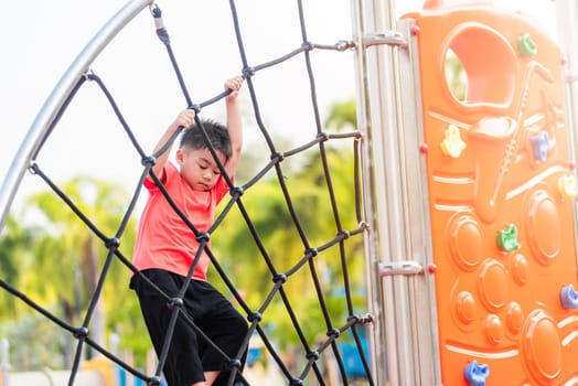Asian child smiling playing climbing outdoor playground, happy preschool little kid having funny while playing climbs on a rope climbing net on playground equipment in daytime in summer, Little boy
