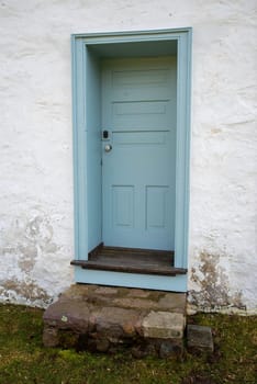 Quaint and charming closed light blue door with stone staps in a whitewashed weathered stone cottage. No people shot outdoors in natural light with copy space.