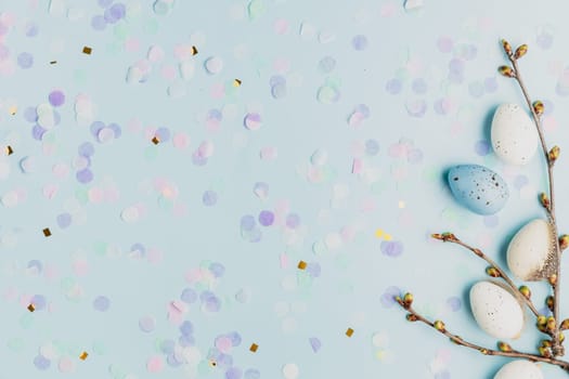 Happy Easter holiday, spring concept. Flat lay with tree branches, flower twigs with white, colorful quail eggs. Blue table background, copy space. Easter home decoration, greeting card, invitation