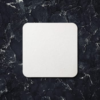 Blank white square beer coaster on black plaster background. Top view.