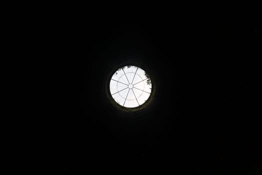 A view of the top of the well from the bottom with the metal grate on the top and the sky with all the black walls around