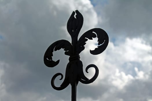 The iron lily on the top of a tower with a dramatic clouded sky in Italy