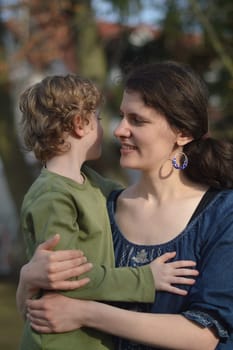Happy mother holding little child in her arms with love in a garden outdoors in summertime