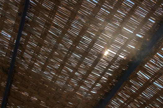 View through palm leaves roof, sun shining behind. Abstract tropical background.