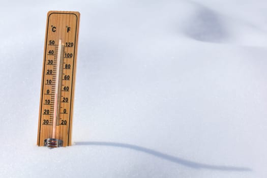 Wooden thermometer standing in the snow, sun casting curvy shadow, red column showing 0 degrees Celsius temperature. Winter / snow coming concept.