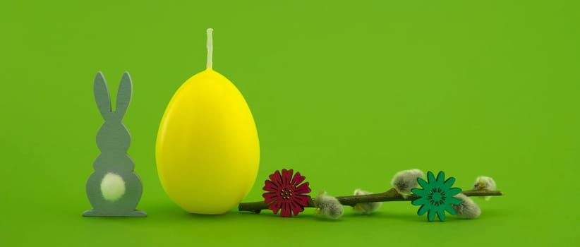 Minimalistic style Easter banner with yellow egg shaped candle, pussy willow branch and Easter Bunny figure over a green background with free copy space for your text