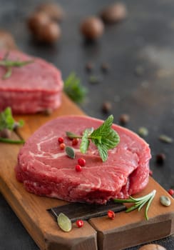 Raw beef fillet steaks on wooden board on dark background close up. Portioned fillet mignons with spices and herbs. Concept of summer food, bbq