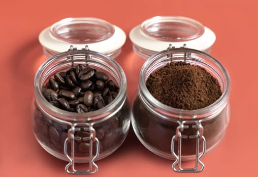 Roasted Coffee beans and grinded coffee in a glass jars close up on pink background. Represent breakfast, energy, freshness or aroma