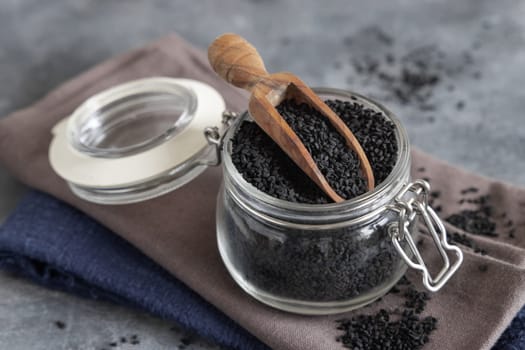Indian spice Black cumin (nigella sativa or kalonji) seeds glass jar with a wooden scoop, close up. Traditional asian medicine, healthy and vegetarian food concept