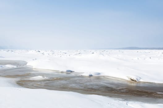 Stunning view of the frozen river covered with chunks of ice and white frosted snow. Snowy desert. The river breaks through the ice.
