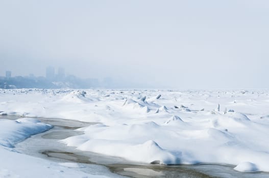 Stunning view of the frozen river covered with chunks of ice and white frosted snow. Snowy desert. The river breaks through the ice.