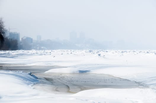 Stunning view of the frozen river covered with chunks of ice and white frosted snow. Snowy desert. The river breaks through the ice.