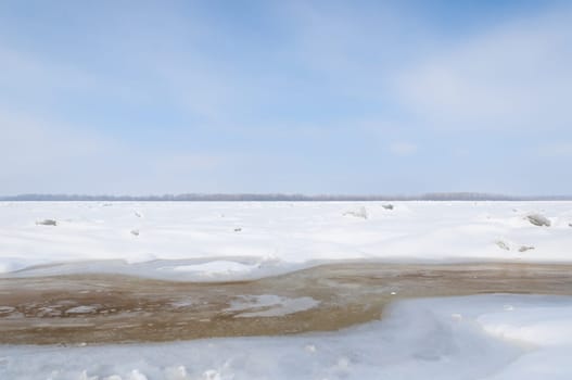 Stunning view of the frozen river covered with chunks of ice and white frosted snow. Snowy desert. The river breaks through the ice.