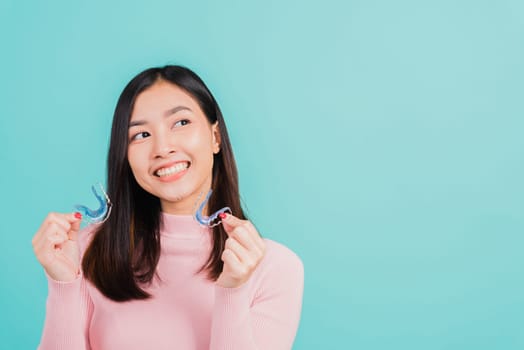 Portrait Asian beautiful young woman smiling hold silicone orthodontic retainers for teeth, Teeth retaining tools after removable braces, isolated blue background, Dental hygiene healthy care concept